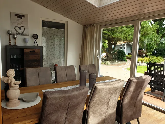 Großer Tisch mit Polsterstühlen im Wintergarten und Blick in den Garten