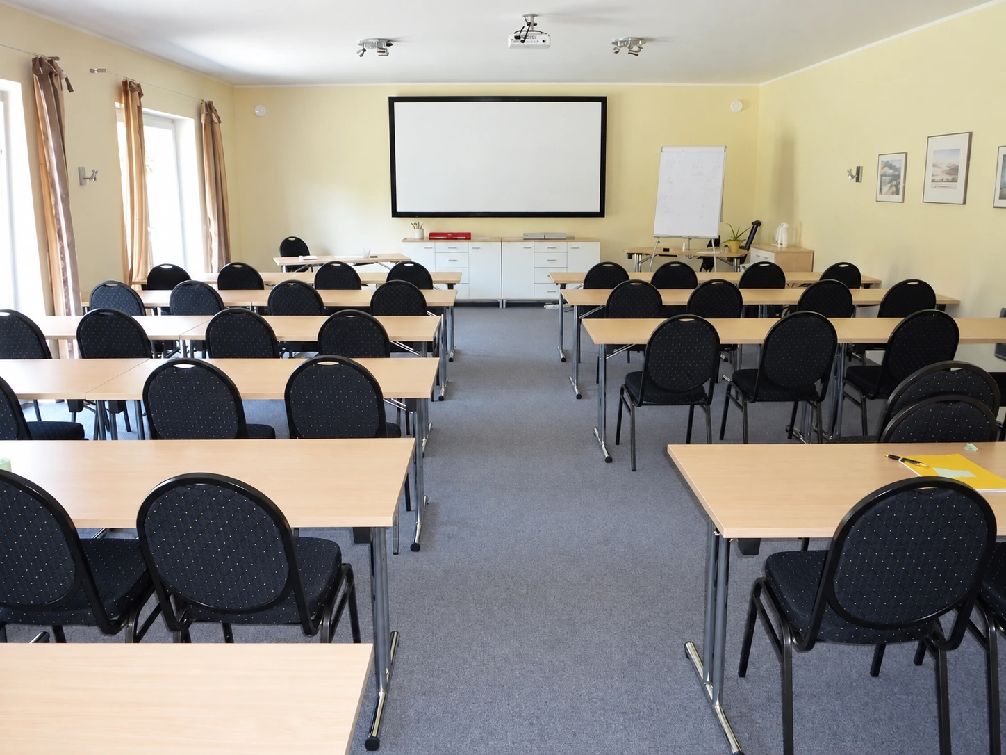 Heller Seminarraum mit Tischen, Stühlen, Beamer und Leinwand